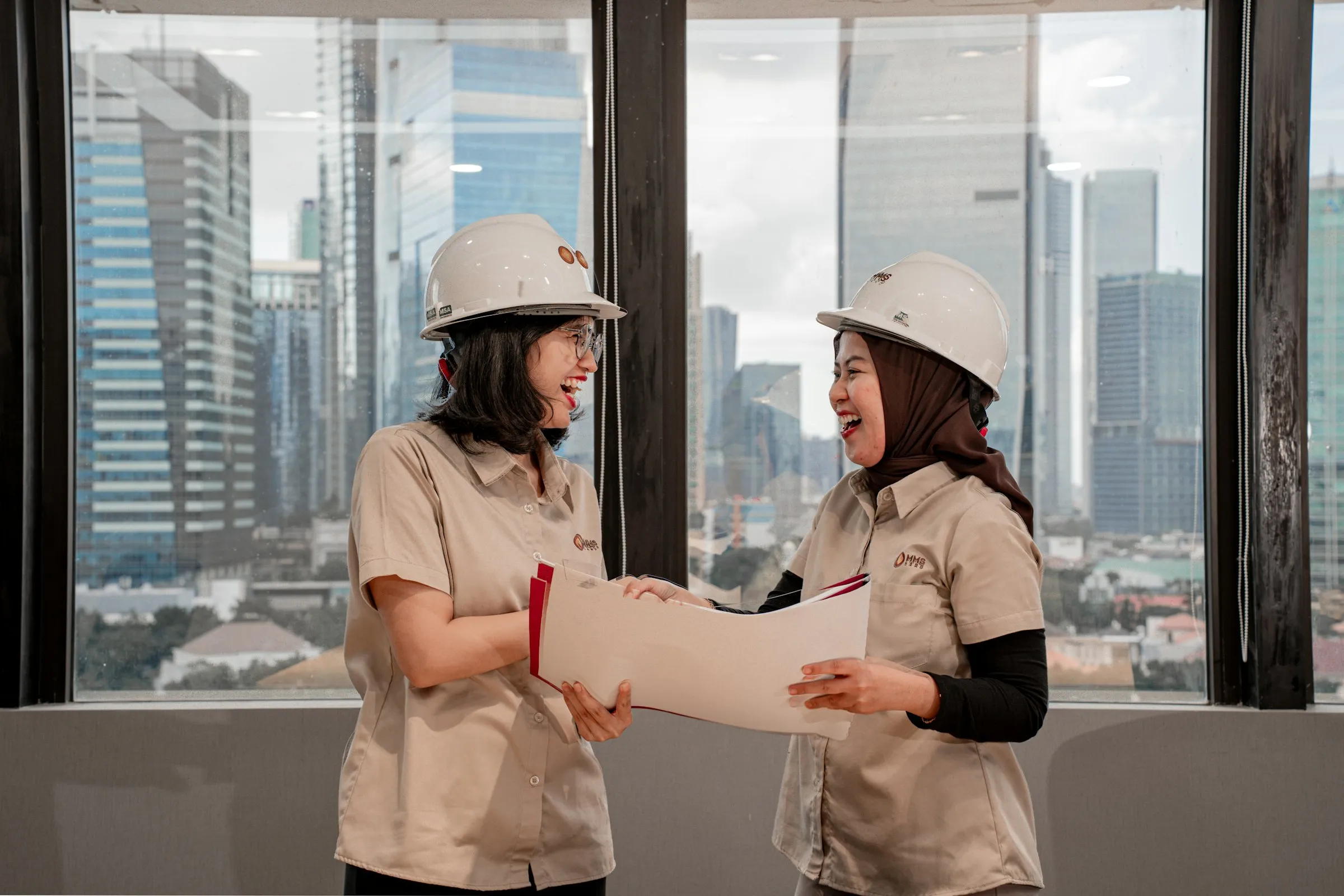 Two engineers in hard hats reviewing project documents above a city skyline