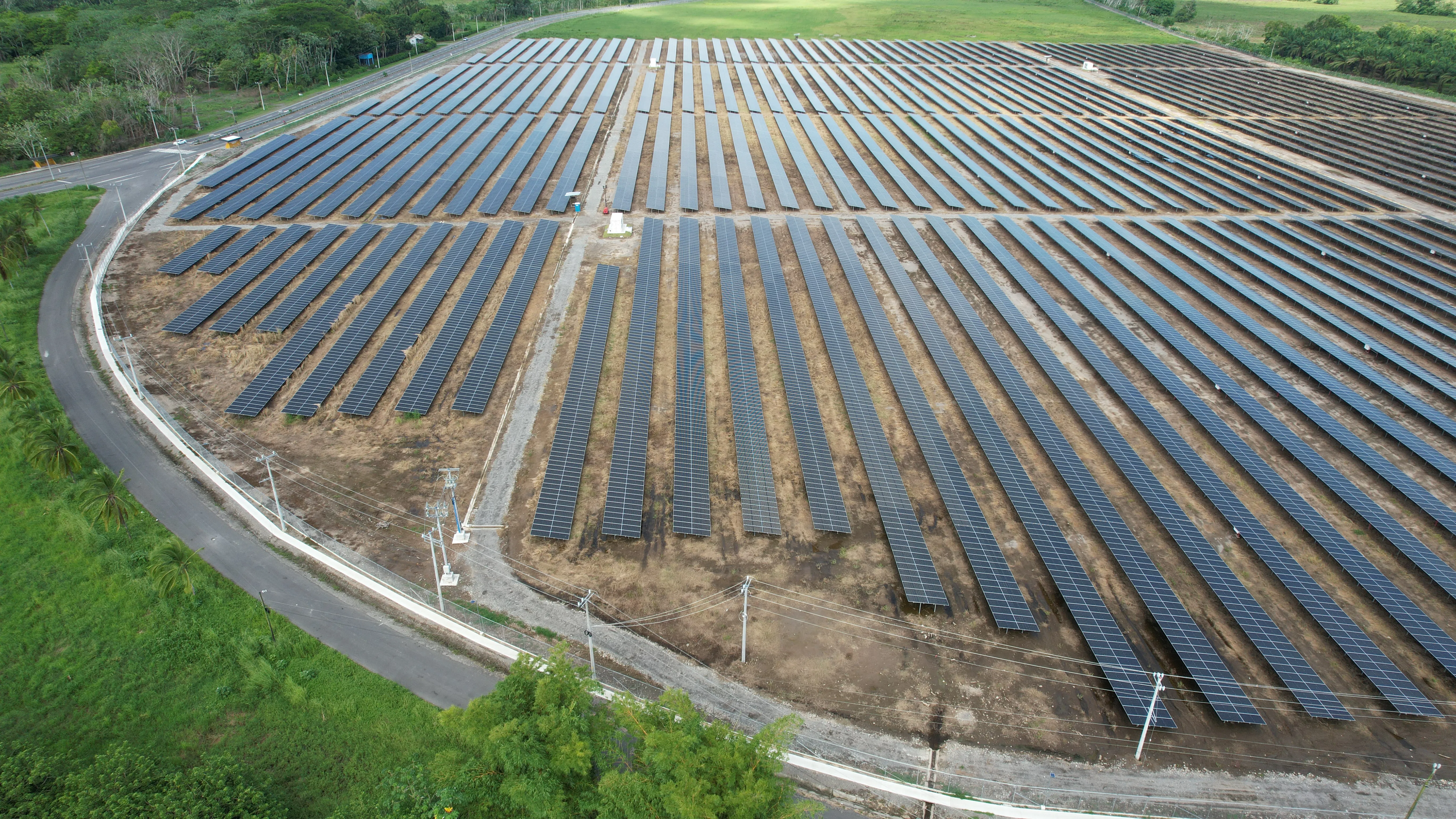 Aerial view of rows of solar panels bounded by a curving access road and power lines